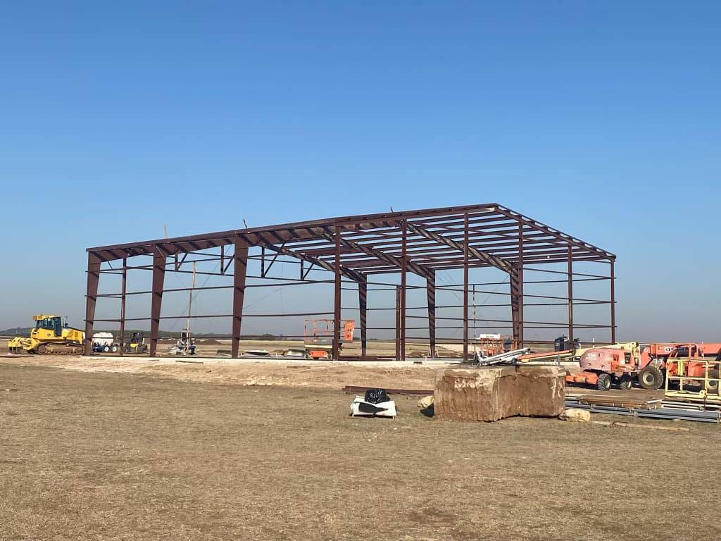 Rust-primed steel building frame skeleton erected in an open Texas field before panel installation