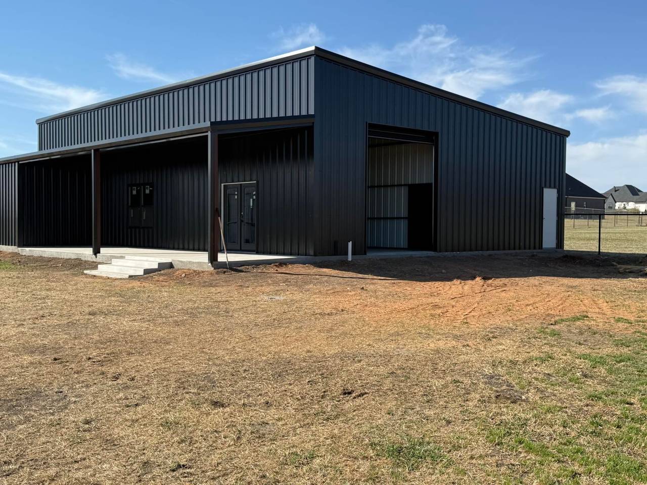 Black steel building with glass French doors and roll-up door, materials supplied by Brazos Metal