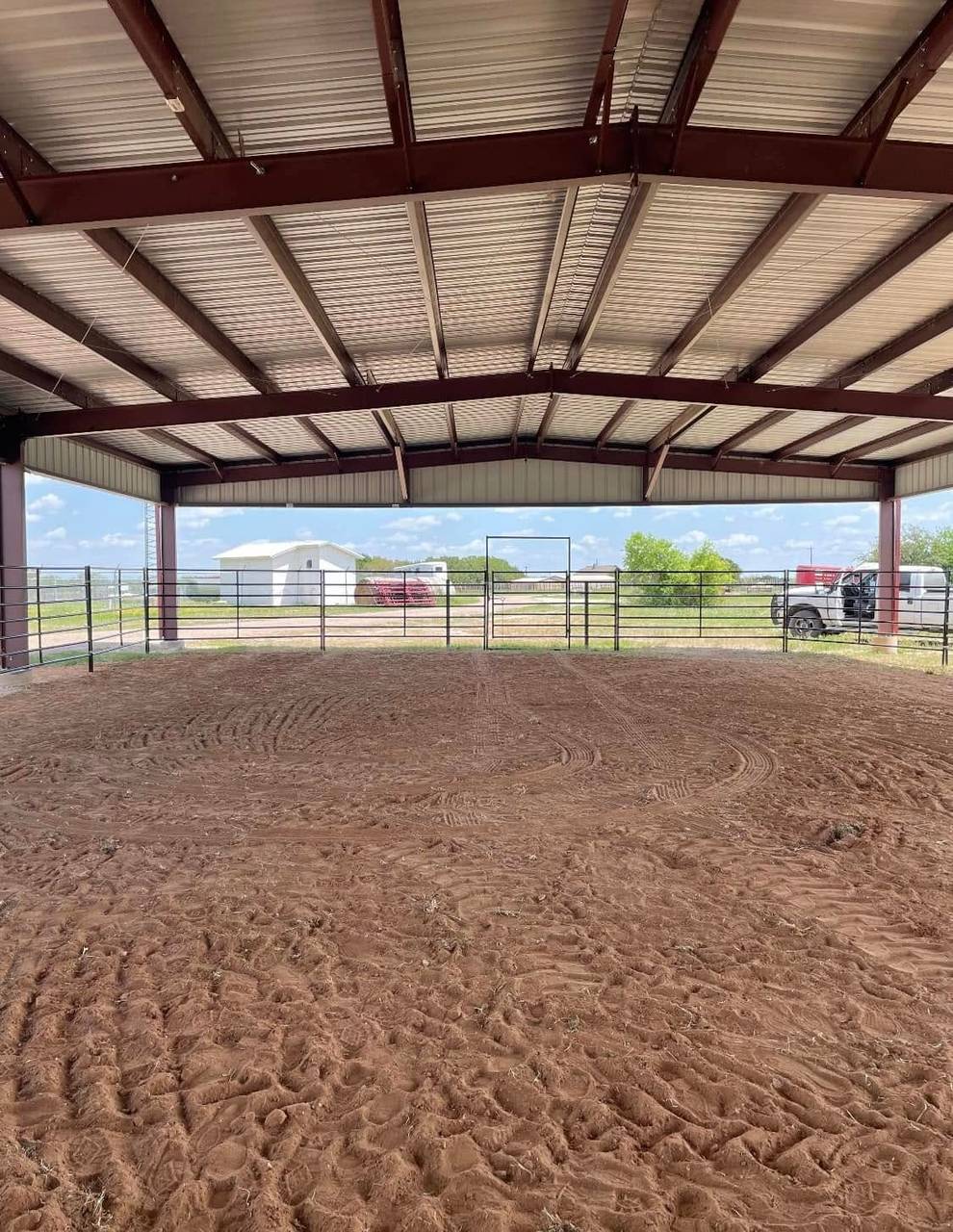 Interior of a covered horse riding arena with dirt floor and open steel-frame sides