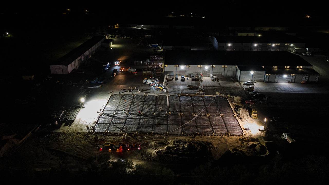 Wide aerial night view of an industrial building complex lit up during active construction
