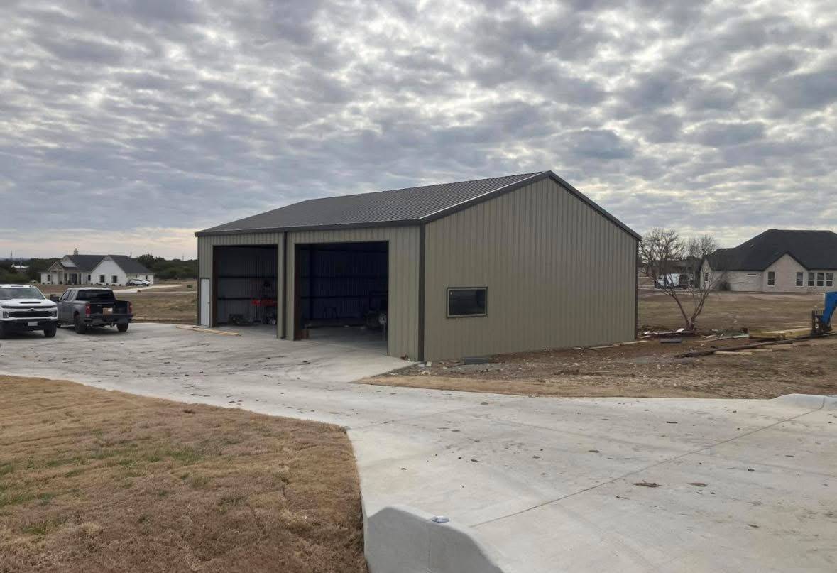 Two-bay tan metal garage and shop building with open doors and concrete driveway